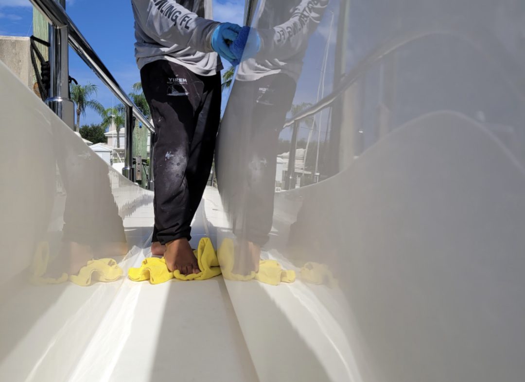 A man in a hoodie is diligently cleaning a boat, ensuring it looks its best for the water.