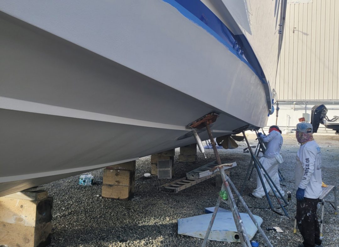 A man carefully paints a boat inside a spacious garage, surrounded by tools and paint supplies.